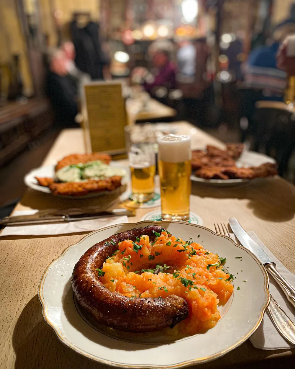 Frische Bratwurst mit Möhren auf einem Teller im Haus Töller, dahinter zwei Kölsch