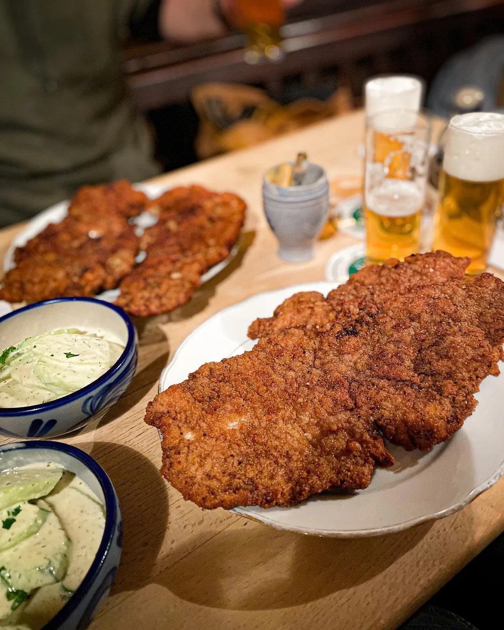 Zwei frisch panierte Schnitzel auf Tellern im Haus Töller, daneben Gurkensalat und Kölsch